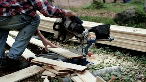 Woodworker operates a miter saw, cutting lumber in a natural outdoor setting Stock Footage 322072183