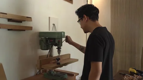 Woodworker operating drill press to bore precise holes in wooden board inside Stock Footage 343898520