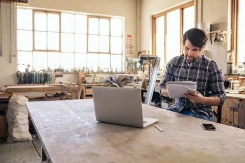 Woodworker reading notes and using a laptop in his workshop Stock Photos