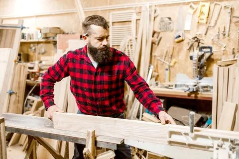 Woodworker shaping a plank in a workshop with tools and equipment during daytime Stock Photos