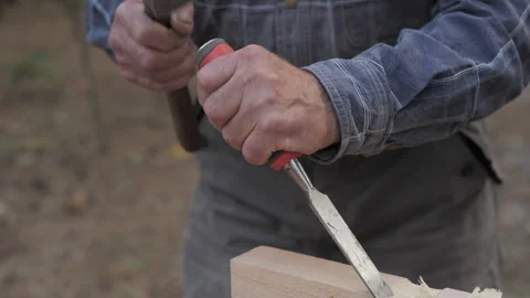 Woodworker shaping a wooden block with chisel and hammer in a serene outdoor Stock Footage 286206987