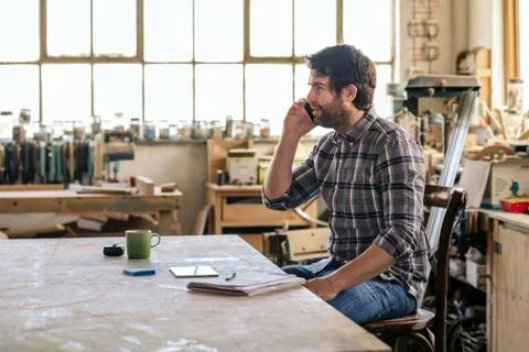 Woodworker sitting at a workbench talking on his cellphone Stock Photos