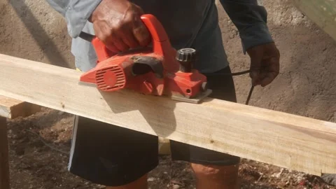 A woodworker uses an electric planer to smooth the surface of a wooden Stock Footage 333345329