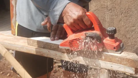 A woodworker uses an electric planer to smooth the surface of a wooden Stock Footage 333345394