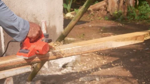 A woodworker uses an electric planer to smooth the surface of a wooden Stock Footage 333348571