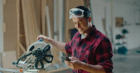 Woodworker using a mobile phone reading a social media chat or texting while Stock Footage 199621666