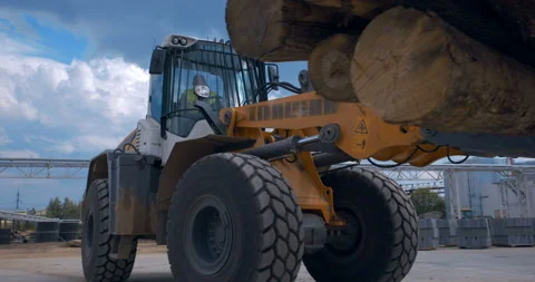 In a woodworking factory, a tractor loader uses a grab to transport a logs Stock Footage 161977251
