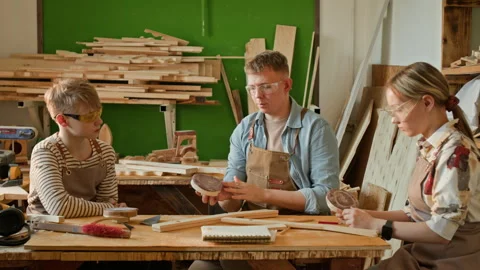 Woodworking Instructor Teaching Two Teenagers to Polish Wood with Hand Sander Stock Footage 334436010