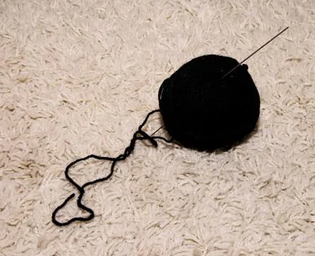 A woolen ball with a black knitting needle lies on a white background Stock Photos
