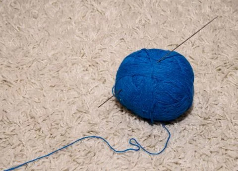 A woolen ball with a blue knitting needle lies on a white background Stock Photos