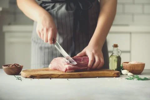 Wooman hands cutting beef meat on wooden chopping board, rosemary, oil, salt Foto stock