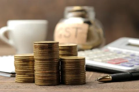 The word GST in the background and a stack of coins with a calculator pen and Stock Photos