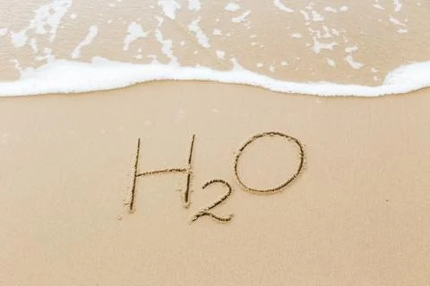 Word H2O written in sand beach, water concept. Stock Photos