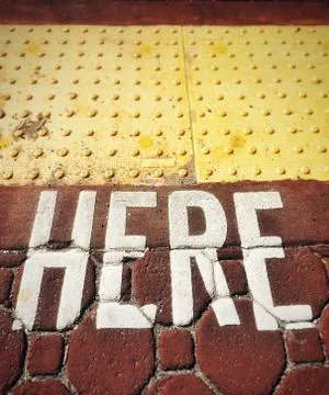 Word HERE painted on to rust colored paving stones. Stock Photos