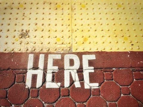 Word HERE painted on to rust colored paving stones. Stock Photos