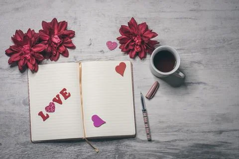 The word "LOVE" on the open notebook page, a pen, flowers, and a cup of coffe Stock Photos
