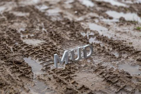 The word mud composed of silver metal letters on wet dirt surface Фото