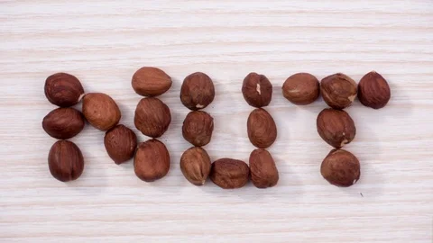 The word NUT made from hazelnuts over light wooden background. Stop motion Stock-Footage 72717045