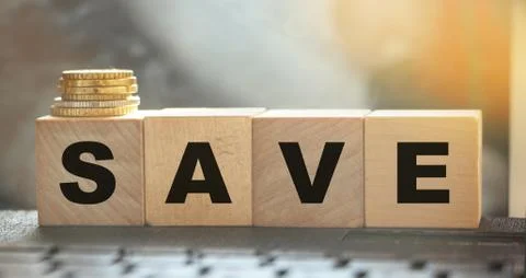 Word Save on wooden cubes on a computer keyboard with coins. Money saving and Stock Photos