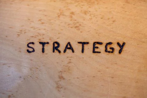 The word strategy handwritten on flat bare plywood surface with woodburner Stockfoto's
