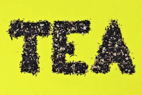 The word tea from black leaf tea on a yellow background. Stock Photos