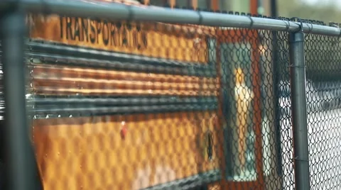 The word "transportation" on the side of a yellow bus, shot from behind a fence. Stock Footage 61298885