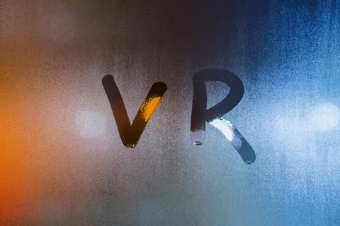 The word vr - virtual reality - written by finger on wet glass with blurred Фото