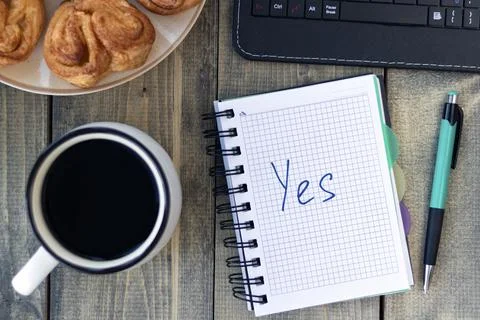 Word Yes in notebook on the working table with cup of coffee and bun. Job rec Stock Photos