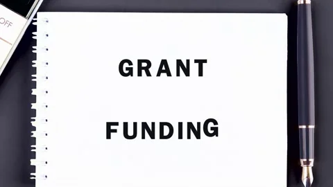 The words GRANT FUNDING are on a notepad next to a sleek pen and calculator. Stock Footage 327187908