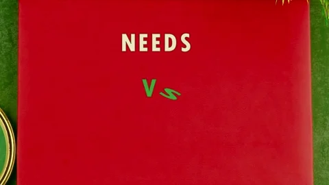 Words NEEDS VS WANTS emerge on a red board set on a green surface Stock Footage 332235668