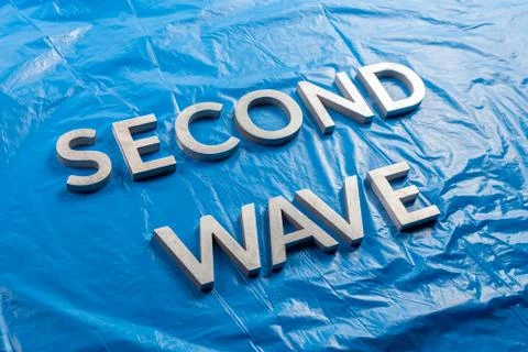 The words second wave laid with silver metal letters over crumpled blue plastic Stock Photos