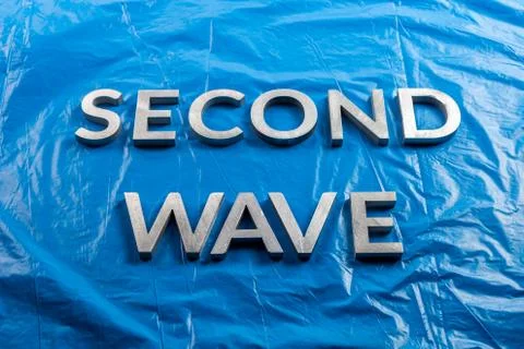 The words second wave laid with silver metal letters over crumpled blue plastic Stock Photos
