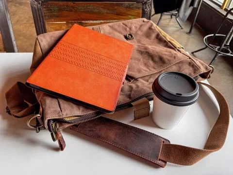 A work bag, tablet, and coffee to go on a coffee shop table Stock Photos