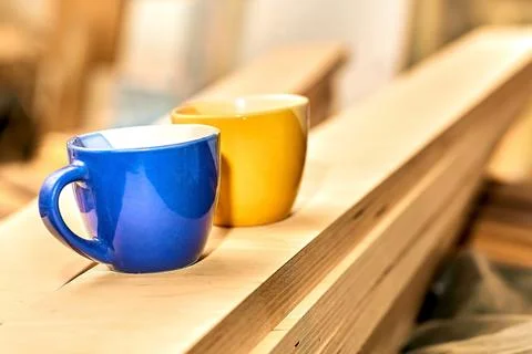 Work break, tea coffee time. Blue and yellow cups in carpentry on wooden planks Stock Photos