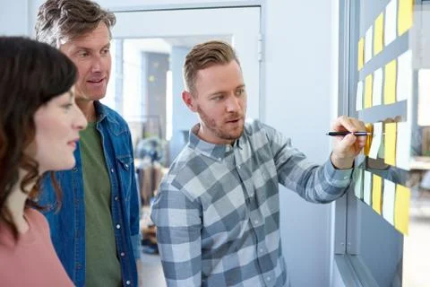 Work colleagues brainstorming with sticky notes on an office wall Stock Photos