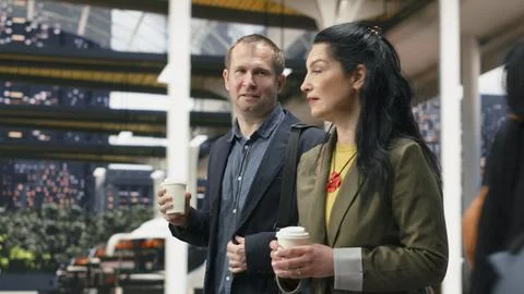 Work colleagues talking and walking inside modern bus terminal, enjoying coffee Stock Photos