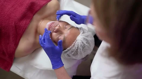 The work of a cosmetologist applying a mask on the face of Asian appearance Stock Footage 231410912