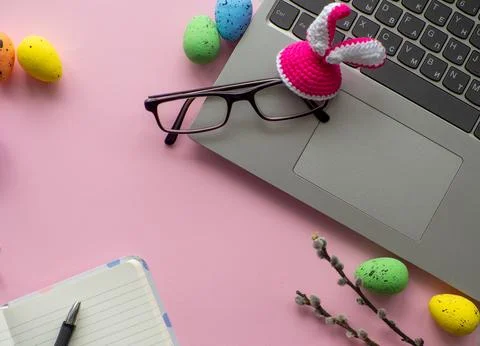Work desk with devices and easter holiday multicolored eggs on pink background Foto stock