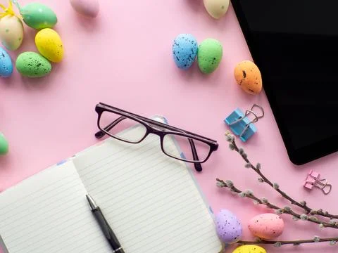 Work desk with devices and easter holiday multicolored eggs on pink background Stock Photos