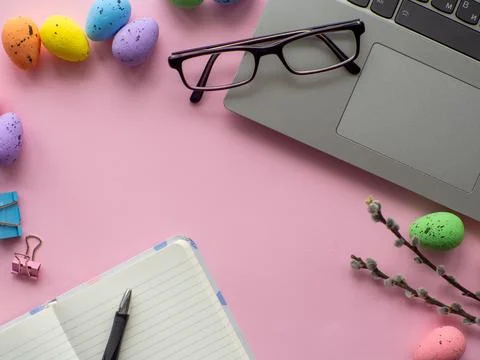 Work desk with devices and easter holiday multicolored eggs on pink background Stock-Fotos
