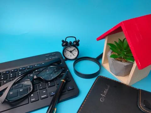 A work desk featuring a model house with a succulent, a keyboard, clock, ma.. 스톡 사진