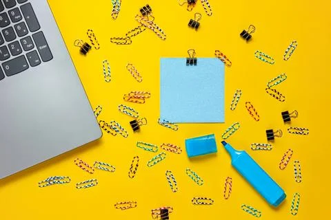 Work desk with laptop, sticky notes, and colorful clips on yellow background Stock Photos