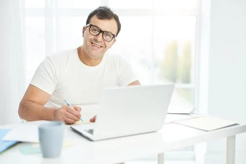 Work at ease. Latin man in white t shirt and eyeglasses smiling at camera while Stock Photos