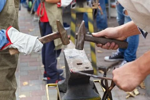 Work with hammers on the anvil in the street forge workshop. Stock Photos