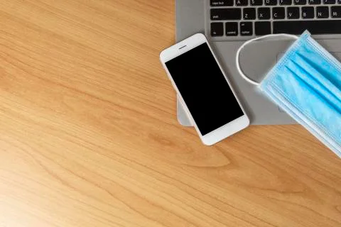 Work from home concept. Top view laptop, smartphone, and face mask on wood ta Stock Photos
