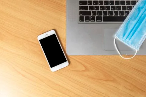 Work from home concept. Top view laptop, smartphone, and face mask on wood ta Stock Photos