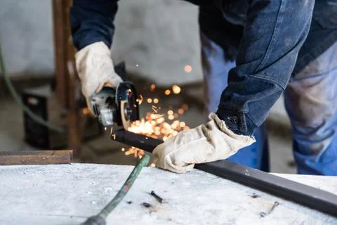 Work at home workshop. Man cuts the metal profile with electric angle grinder Foto stock