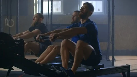 Work on the muscles of the back. Three Men working out on rowing machine in gym Stock Footage 124473942
