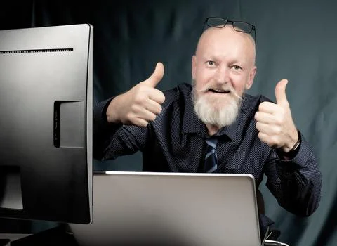 Work in the office, a cheerful elderly man with a gray beard in front of a Stock Photos