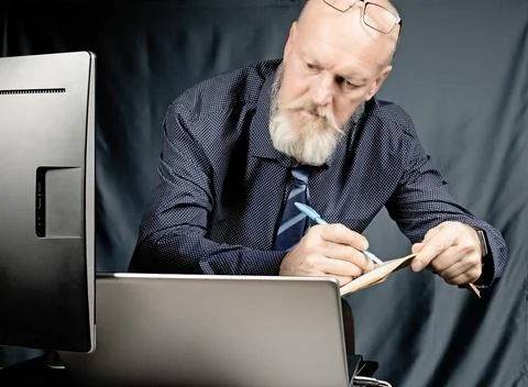 Work in the office, a serious elderly man with a gray beard in front of a laptop Stock Photos